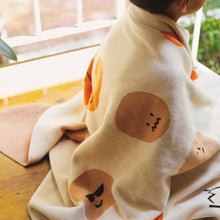 Load image into Gallery viewer, Child sitting with the My Feelings kids blanket wrapped around them, showing playful graphic faces expressing various emotions in earthy tones