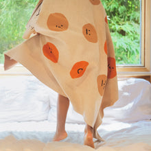 Load image into Gallery viewer, Child walking with the My Feelings kids blanket draped over their shoulders, showing playful orange-toned facial expression graphics