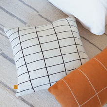 Load image into Gallery viewer, Modern grid cotton knit pillow cover in black and cream styled on a neutral rug beside an orange windowpane pillow for a cozy, minimal look