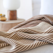 Load image into Gallery viewer, Close-up of ribbed cotton knit throw blanket in cacao and oat milk tones draped on a neutral bed with soft natural lighting