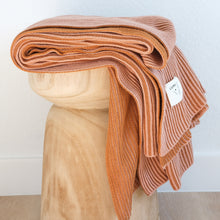 Load image into Gallery viewer, Folded ribbed knit cotton throw blanket in burnt orange and pink clay on a carved wooden stool with Lumi Living label