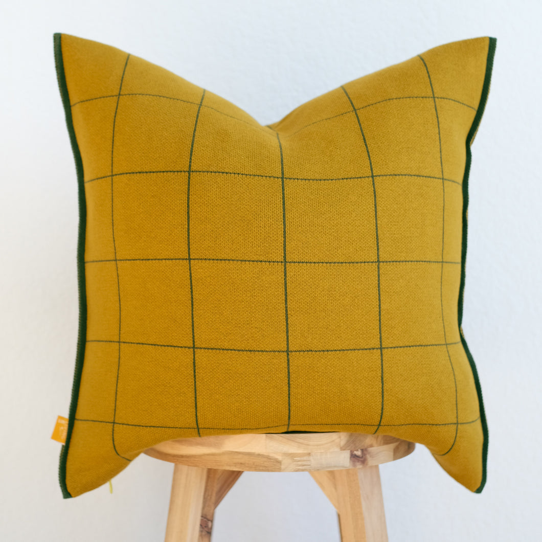 Windowpane knit pillow cover in Mustard background with dark green lines on natural wood chair