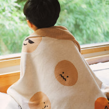 Load image into Gallery viewer, Child sitting by a window wrapped in a cotton knit blanket featuring expressive cartoon emotion faces in soft beige tones
