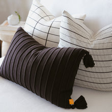 Load image into Gallery viewer, Black ribbed lumbar pillow with tassels styled alongside modern grid cotton pillow covers in small and medium patterns on a white sofa
