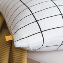 Load image into Gallery viewer, Close-up of modern grid cotton knit pillow cover in black and cream with corner tag detail, styled on a sofa with a mustard knit throw

