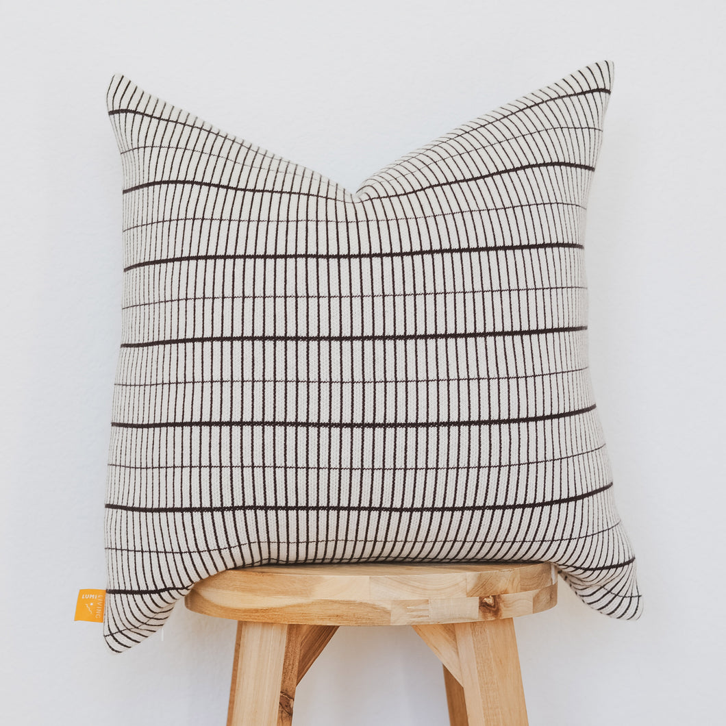 Small grid black and cream cotton knit pillow cover displayed on wooden stool against white background
