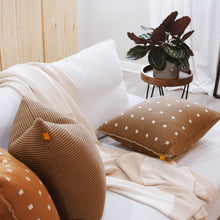 Load image into Gallery viewer, Burnt orange and mocha brown checkered knit pillow covers styled on a cozy white sofa, paired with a ribbed accent pillow and cream knit throw, next to a leafy potted plant.
