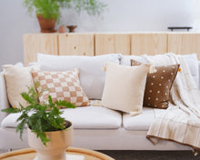 Load image into Gallery viewer, Neutral-toned knit throw pillows in checkered, ribbed, and dotted patterns styled on a white sofa with a cream knit throw, light wood decor in the background, and a potted fern in the foreground.
