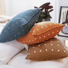 Load image into Gallery viewer, Stack of three modern knit pillow covers in teal, burnt orange, and cocoa brown, each with a small white checker pattern, styled on a neutral couch with soft natural light.
