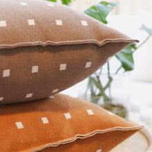 Load image into Gallery viewer, Close-up of cocoa brown and burnt orange cotton knit pillow covers with white square checker patterns and piped edges, styled with greenery in the background.
